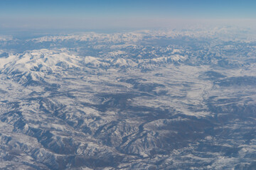 Wing of aerial view of an airplane jet flying above clouds from the window in traveling and transportation concept. White snow mountain in winter season. Nature landscape background.