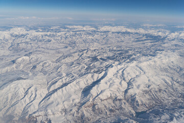 Obraz premium Wing of aerial view of an airplane jet flying above clouds from the window in traveling and transportation concept. White snow mountain in winter season. Nature landscape background.