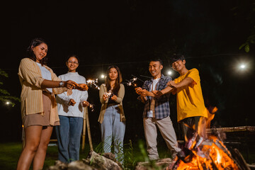 a group of people so excited while playing with the fireworks around the bonfire at the camp site