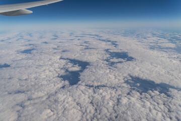 Naklejka na ściany i meble Wing of aerial view of an airplane jet flying above clouds from the window in traveling and transportation concept. White snow mountain in winter season. Nature landscape background.