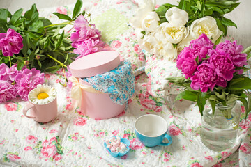 Delicate bouquets of peony flowers, gift boxes and sweets on a colorful vintage bedspread.