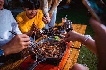 the group of people grilling the beef and the onions using the grilled pan and chopsticks at the camp site