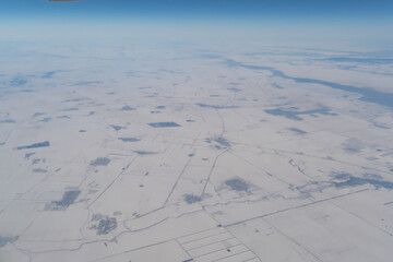Wing of aerial view of an airplane jet flying above clouds from the window in traveling and transportation concept. White snow mountain in winter season. Nature landscape background.