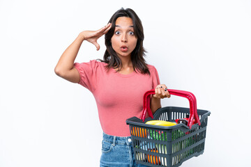 Young woman holding a shopping basket full of food with surprise expression