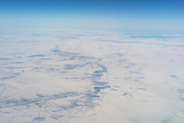 Wing of aerial view of an airplane jet flying above clouds from the window in traveling and transportation concept. White snow mountain in winter season. Nature landscape background.