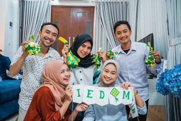 five smiling young people holding a chain of eid mubarak flags and decorations as they gather at home