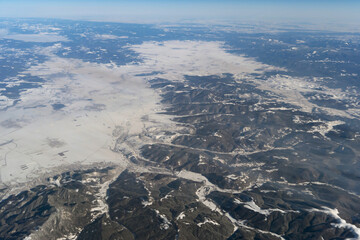 Wing of aerial view of an airplane jet flying above clouds from the window in traveling and transportation concept. White snow mountain in winter season. Nature landscape background.