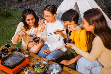 the guy in yellow t shirt and woman in white long sleeved t shirt eating the grilled beef using the chopsticks while woman in cardigan eating using the spoon