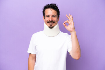 Young caucasian man wearing neck brace isolated on purple background showing ok sign with fingers