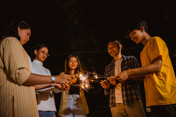 a group of people standing in circle while playing with the fireworks happily at the camp site