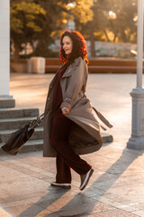 Outdoor fashion portrait of young elegant fashionable brunette woman, model in stylish hat, choker and light raincoat posing at sunset in European city.