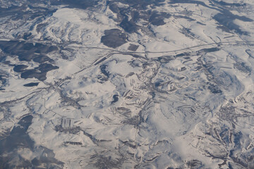 Wing of aerial view of an airplane jet flying above clouds from the window in traveling and transportation concept. White snow mountain in winter season. Nature landscape background.