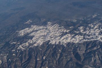 Wing of aerial view of an airplane jet flying above clouds from the window in traveling and transportation concept. White snow mountain in winter season. Nature landscape background.