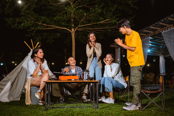 a group of people sitting together while looking at the guy in yellow t shirt that standing and put his hands together