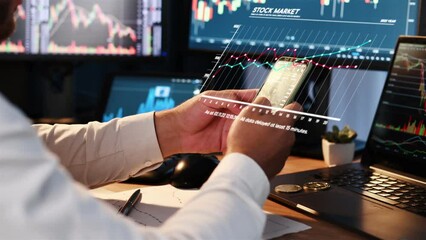 Close up view of phone with stock exchange information that is holding by office worker. Many displays with graphs.