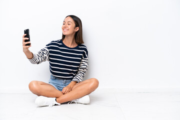 Young caucasian woman sitting on the floor isolated on white background making a selfie