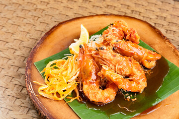 Deep fried prawns with tamarind sauce on banana leaf and wooden plate with sliced egg, fried noodles and lime.