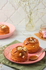Obraz na płótnie Canvas Yeast dough cruffins with salted caramel and hazelnuts on a pink plate on a light wooden background.