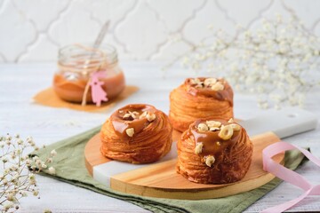 Obraz na płótnie Canvas Yeast dough cruffin with salted caramel and hazelnuts on a wooden board on a light wooden background. Easter baking concept.