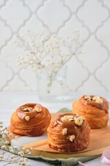 Yeast dough cruffin with salted caramel and hazelnuts on a wooden board on a light wooden background. Easter baking concept.