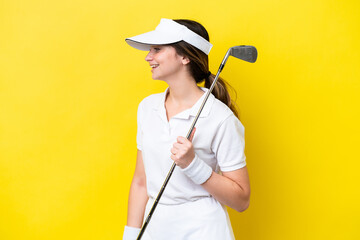 young caucasian woman playing golf isolated on yellow background laughing in lateral position
