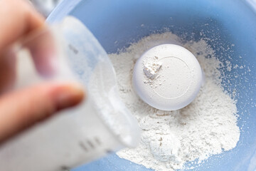 The hand pours flour from a measuring cup, a round-shaped cake is obtained. Close-up