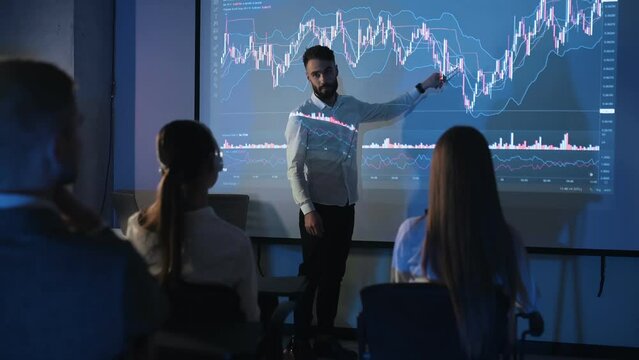 Stock trading graphs. Man in formal clothes is showing business plan on the big projector for the people.
