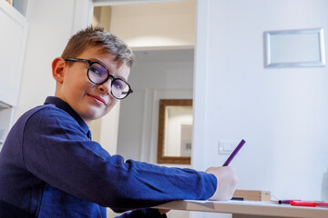 Bambino biondo con gli occhiali e una polo blu fa i compiti nella sua camera