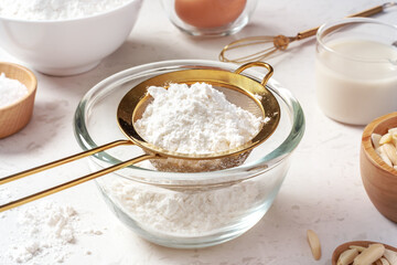 Fototapeta na wymiar Sifting flour with gold sieve in glass bowl, closeup