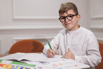 Bambino biondo con gli occhiali   fa i compiti seduto in una scrivania a casa 