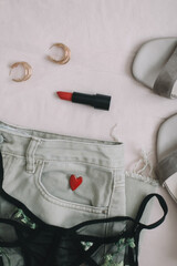 Overhead view of woman's casual spring outfit with phone or tablet, jeans, sandals, underwear, red lipstick and earrings on beige background, Flat lay, top view