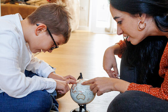 Una mamma con i capelli scuri mostra al figlio un mappamondo seduti nel pavimento di casa
