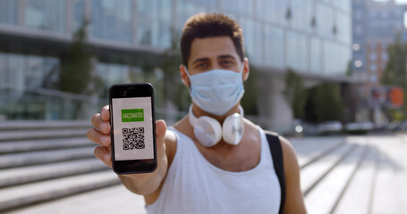 Sportsman in safety mask showing at camera cellphone with vaccination certificate for covid-19.
