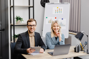 Start up business team on meeting in modern office interior, working on laptop and tablet. A young woman and a man are sitting at the table and working on a business project