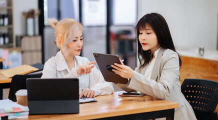 Two Asian businesswoman discuss investment project working and planning strategy with tablet laptop computer in office...