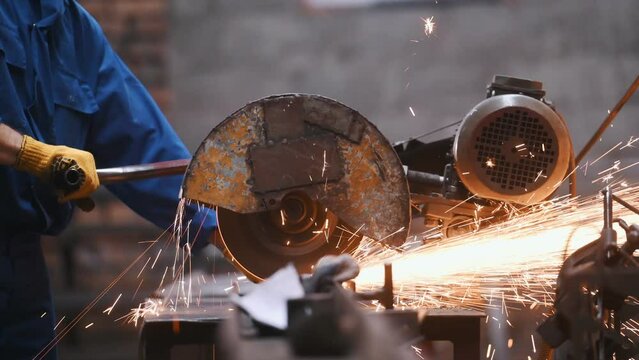 Cutting the metal by saw. Close up view. Factory male worker in uniform is indoors.