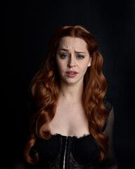 Fototapeta premium close up portrait of beautiful woman with long red hair wearing sheer corset top. variety of facial expressions, Isolated on dark studio background with moody silhouette lighting.