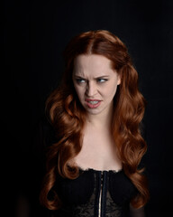 close up portrait of beautiful woman with long red hair wearing sheer corset top. variety of facial expressions,  Isolated on dark studio background with moody silhouette lighting.