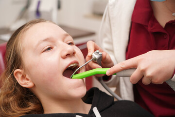 The girl is sitting on a dental chair, the doctor performs various manipulations in the girl's...