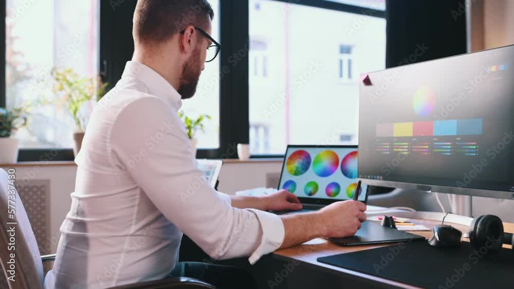 Poster uses a graphics tablet with a stylus. male graphic designer is working by computer in the office.