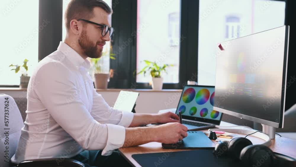 Poster uses a graphics tablet with a stylus. male graphic designer is working by computer in the office.