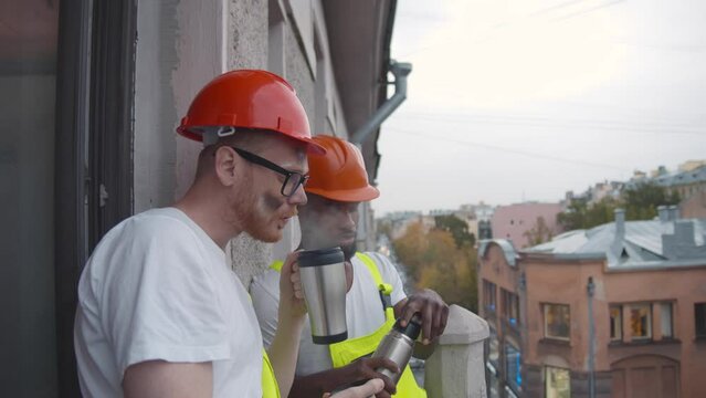 Diverse builders drink coffee during break at construction site. Realtime