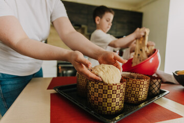 mom with her little sons at the table in the kitchen at home preparing together the dough for baking a holiday cake