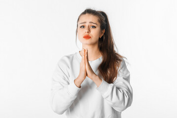 Please. Hopeful young woman showing begging gesture, asking for favour, standing over white background. Brunette girl wishing something, praying for luck or asking something