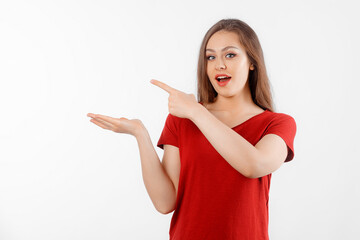 Surprised lovely girl points left at promo banner, shows advertisement on blank white space. Young brunette female looking amazed by promotion offer, stands over white background