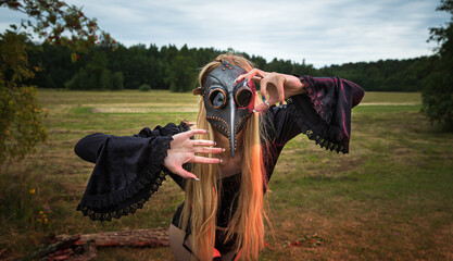 Intriguing portrait of woman in crow mask with forest background.