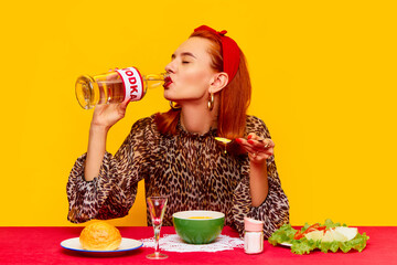 Beautiful redhead woman sitting at table against yellow background and having dinner with cheese,...