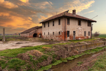 Fototapeta na wymiar Old abandoned farmhouse with typical rural architecture of the Po Valley in the province of Cuneo, Italy, at sunset