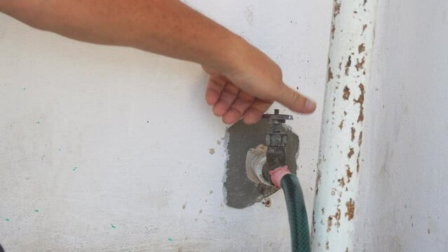 A man closes an old faucet in the wall with a hose attached