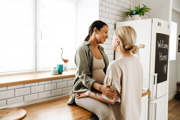 Cheerful lesbian couple hugging while spending time together in kitchen